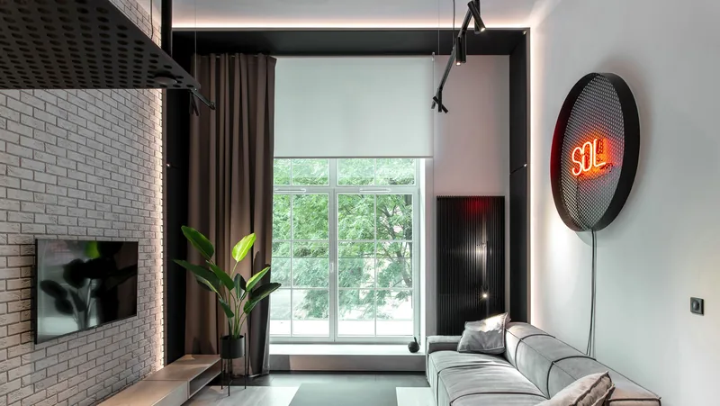 Salon w kamienicy z reflektorami na szynie i ceglaną ścianą, wysokie okno i szara sofa — Chors