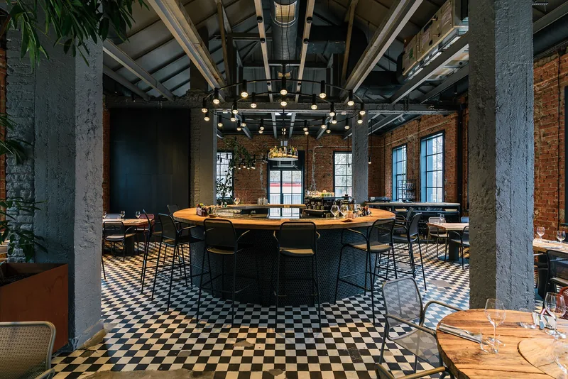 Wnętrze restauracji w starej hali: okrągły bar, ceglane ściany, pierścień z punktowych zwisów pod dachem — Chors