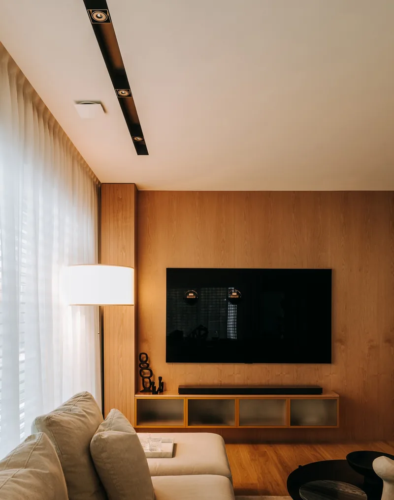Lampa podlogowa z bialym abazurem obok strefy telewizyjnej w salonie z drewniana sciana