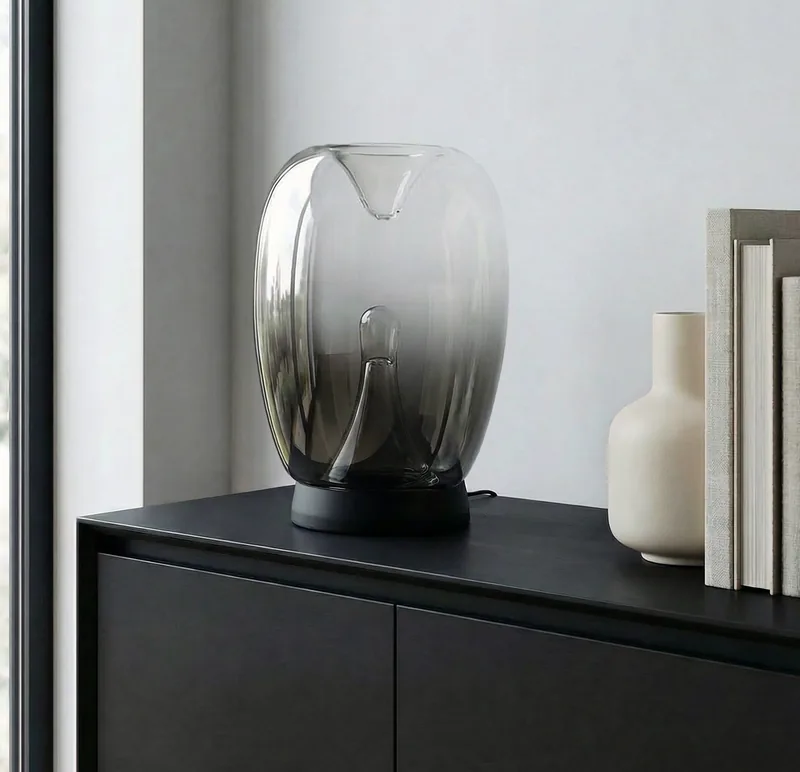 Szklana lampa stolowa w dymnym kloszu na czarnej komodzie w salonie